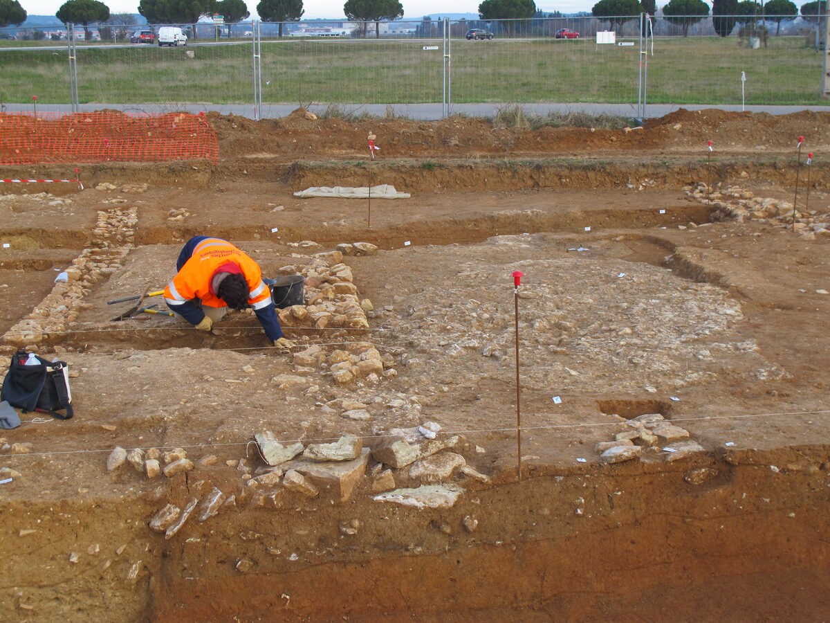 Archéologues de l'Inrap en train de fouiller une surface décapée, accroupis au-dessus de structures dégagées dans le sol